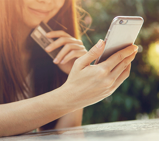 Woman using smartphone with debit card in other hand