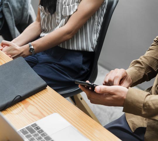 showing hands of man and woman at desk and man on smartphone